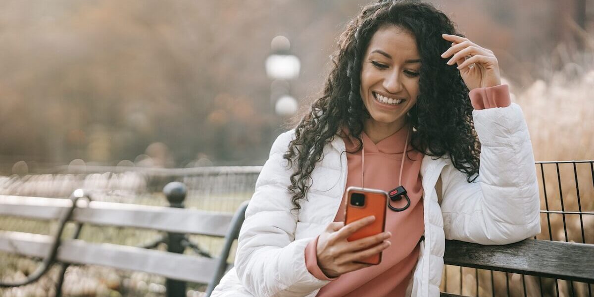 smiling woman with smartphone on park bench